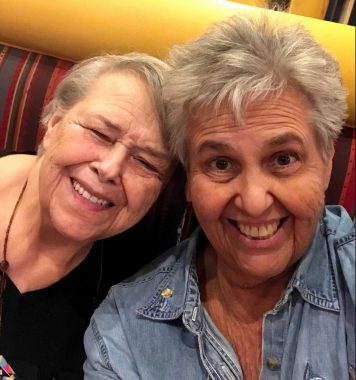 Parkinson's hero | Parkinson's News Today | Sisters Bev and Jo Gambosi wear broad smiles while taking a selfing on a colorful yellow booth with red and orange stripes. They look very sweet and mischievous.