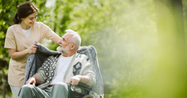 A female caregiver walking and talking with an older man in a wheelchair