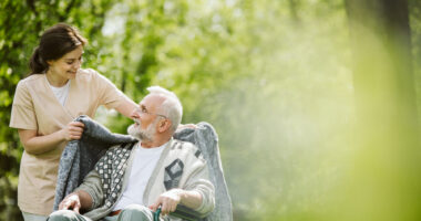 A female caregiver walking and talking with an older man in a wheelchair