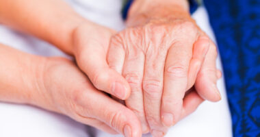 Young caregiver holding hand of elderly person