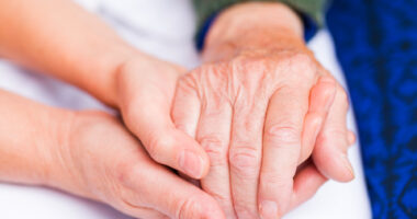 Young caregiver holding hand of elderly person