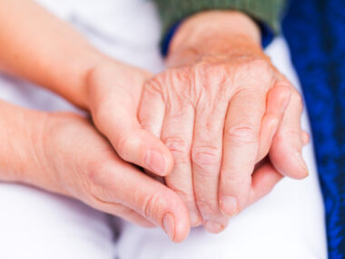 Young caregiver holding hand of elderly person