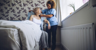 A female caregiver helping a female patient get out of bed and get dressed