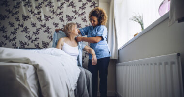 A female caregiver helping a female patient get out of bed and get dressed