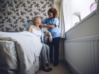 A female caregiver helping a female patient get out of bed and get dressed