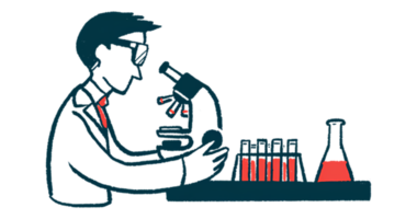 A scientist looks through a microscope on a lab table, alongside a beaker and a rack of test tubes.