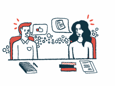 Two people talk while seated next to each other at a table.