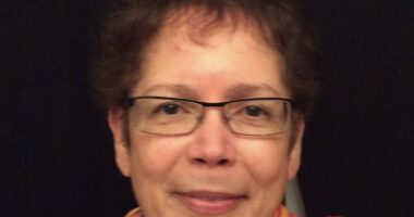 A close-up photo shows a woman with short brown hair and glasses.