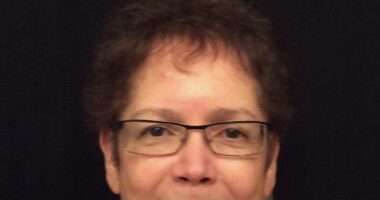 A close-up photo shows a woman with short brown hair and glasses.