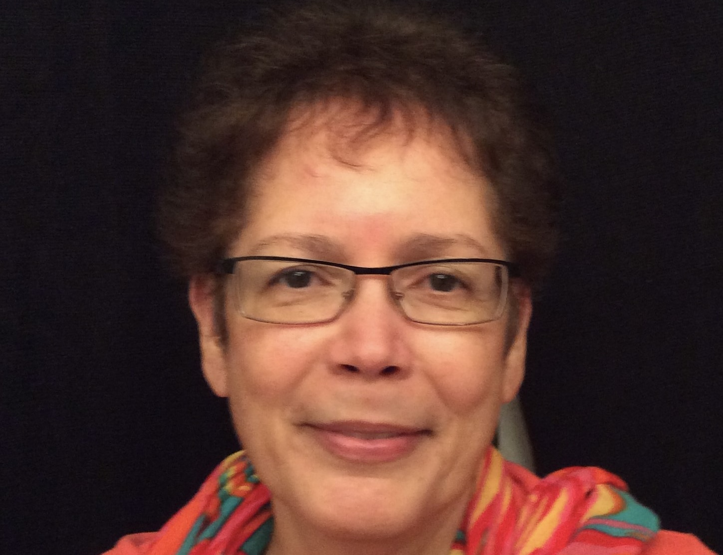 A close-up photo shows a woman with short brown hair and glasses.