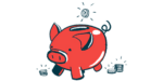 A coin is seen just above the slot on a pig-shaped bank.